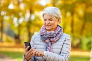 technology, old age and people concept - happy senior woman with smartphone at autumn park. happy senior woman with smartphone at autumn park
