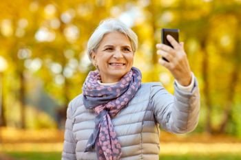 old age, retirement and technology concept - happy senior woman taking selfie by smartphone at autumn park. senior woman taking selfie at autumn park