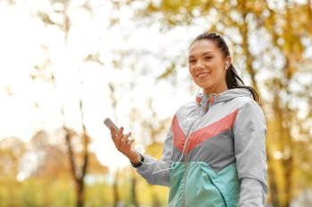 fitness, sport, people and healthy lifestyle concept - young woman with earphones and smartphone in autumn park. woman in autumn park and listening to music