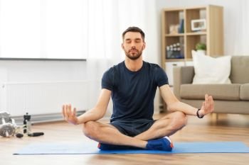 sport, fitness and healthy lifestyle concept - man meditating in lotus pose on yoga mat at home. man meditating in lotus pose on yoga mat at home