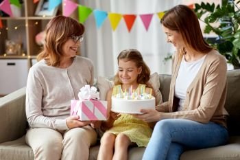 family, generation and celebration concept - smiling mother, daughter and grandmother with gift box and birthday cake with ten candles at home. mother, daughter and grandmother on birthday