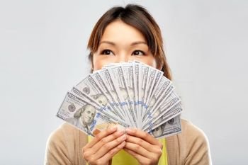 people, ethnicity and portrait concept - happy asian young woman holding hundreds of dollar money banknotes over grey background. asian woman with hundreds of dollar money