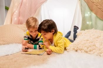 childhood, travel and hygge concept - happy little boys with magnifier and road map searching location in kids tent at home. boys with magnifier and map in kids tent at home