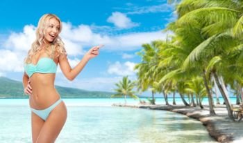summer holidays, vacation and travel concept - happy smiling young woman in bikini swimsuit pointing finger over tropical beach background in french polynesia. happy smiling young woman in bikini on beach