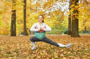 fitness, sport, people and healthy lifestyle concept - young woman stretching leg at autumn park. young woman doing sports at autumn park
