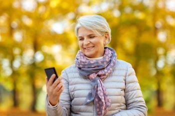 technology, old age and people concept - happy senior woman with smartphone at autumn park. happy senior woman with smartphone at autumn park