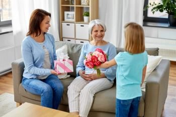 family, generation and birthday - happy mother with gift box and daughter giving flowers to grandmother at home. granddaughter giving flowers to grandmother