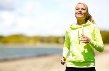 fitness, sport and healthy lifestyle concept - smiling woman running over summer beach background. smiling woman running along beach