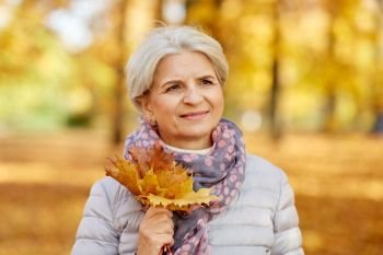 old age, retirement and season concept - portrait of happy senior woman with maple leaves at autumn park. senior woman with maple leaves at autumn park