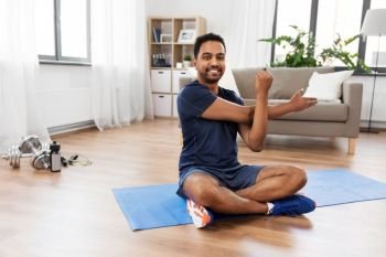 sport, fitness and healthy lifestyle concept - indian man training and stretching arm at home. man training and stretching arm at home