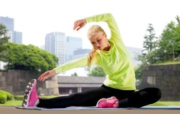 fitness, sport and healthy lifestyle concept - woman stretching on exercise mat over summer park in tokyo city background. woman stretching on exercise mat at city park
