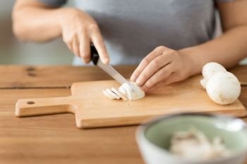 cooking, culinary and edible mushrooms concept - close up of woman chopping champignons by kitchen knife on wooden cutting board. woman cutting champignons by knife on board