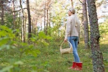 season, nature and leisure concept - young woman with mushrooms in basket walking along autumn forest. young woman picking mushrooms in autumn forest