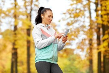 fitness, sport, people and healthy lifestyle concept - young woman with earphones and smartphone in autumn park. woman in autumn park and listening to music