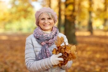 old age, retirement and season concept - portrait of happy senior woman with maple leaves at autumn park. senior woman with maple leaves at autumn park