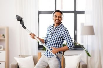 household and cleaning concept - indian man in headphones with vacuum cleaner having fun at home. man in headphones with vacuum cleaner at home