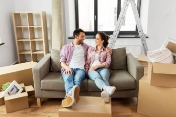 moving, people, repair and real estate concept - happy couple with cardboard boxes sitting on sofa at new home. happy couple with boxes moving to new home