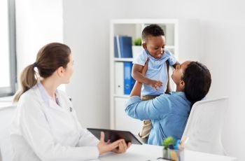 medicine, healthcare and pediatry concept - african american mother with baby son and caucasian doctor with tablet computer at clinic. mother with baby and doctor with tablet at clinic