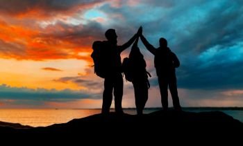 travel, tourism and hike concept - group of travelers with backpacks making high five over sunset background. travelers making high five over sunset