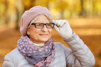 old age, retirement and season concept - portrait of happy senior woman in glasses at autumn park. portrait of happy senior woman at autumn park