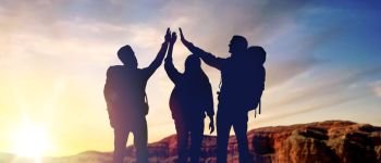 travel, tourism and hike concept - group of travellers with backpacks making high five over sunrise at grand canyon national park background. travellers making high five over sunrise
