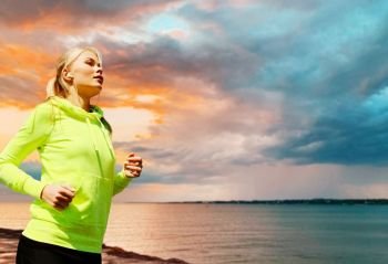 fitness, sport and healthy lifestyle concept - woman with earphones running and listening to music over sea sunset background. woman with earphones running over sea sunset