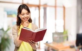 education and business concept - happy asian young woman reading book over office background. happy asian woman reading book at office
