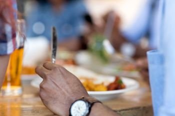 leisure, food and people concept - close up of african american man eating with friends at restaurant. african man eating with friends at restaurant