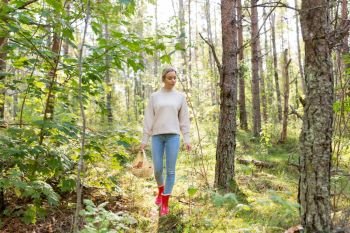 season, nature and leisure concept - young woman with mushrooms in basket walking along autumn forest. young woman picking mushrooms in autumn forest