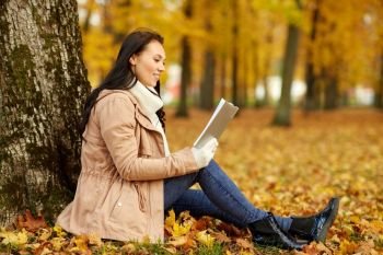 season, technology and people concept - young woman reading book at autumn park. woman reading book at autumn park