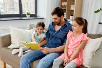 family, leisure and people concept - happy father with daughters reading book at home. happy father with daughters reading book at home