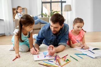 family, motherhood and leisure concept - father spending time with her little daughters drawing and helping with homework lying on floor at home. father spending time with little daughters at home