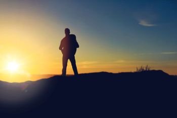 travel, tourism, hike and people concept - traveller with backpack standing on edge of hill over sunrise background. traveller standing on edge of hill over sunrise