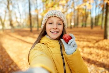 season and people concept - happy girl with apple taking selfie at autumn park. happy girl with apple taking selfie at autumn park