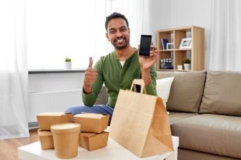 technology, consumption and people concept - smiling indian man using smartphone for food delivery and showing thumbs up at home. indian man using smartphone for food delivery