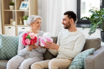family, mother’s day and birthday concept - smiling adult son giving present and flowers to his senior mother at home. son giving present and flowers to senior mother