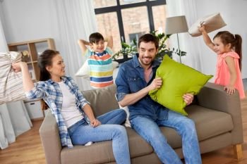 family, childhood and people concept - happy father, mother, little son and daughter fighting by pillows and having fun at home. happy family having pillow fight at home