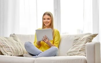 people, technology and leisure concept - happy young woman or teenage girl sitting on sofa with tablet pc computer at home. young woman or teenage girl with tablet pc at home