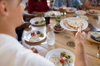 leisure, food and people concept - group of happy international friends eating at restaurant and male hand holding plate with chapati bread. international friends eating at restaurant