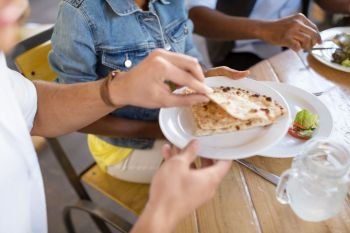 leisure, food and people concept - group of happy international friends eating at restaurant and male hand holding plate with chapati bread. international friends eating at restaurant