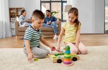 childhood, leisure and family concept - brother and sister playing with wooden toy blocks at home. brother and sister playing toy blocks at home