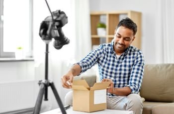 mail delivery, shipment and blogging concept - happy indian male blogger opening parcel box and recording unboxing video with camera at home. male video blogger opening parcel box at home
