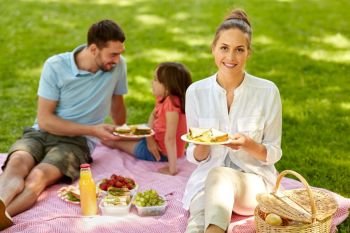 family, leisure and people concept - happy mother, father and daughter having picnic at summer park. happy family having picnic at summer park