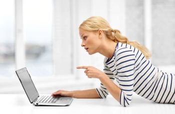 communication, technology and people concept - displeased young woman having video call and pointing finger to laptop computer at home. woman having video call on laptop computer at home