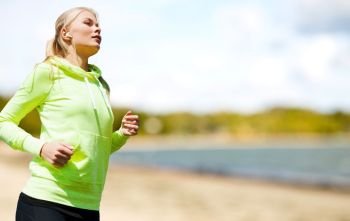 fitness, sport and healthy lifestyle concept - woman with earphones running and listening to music over summer beach background. woman with earphones running at park