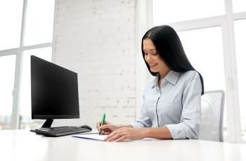business, education and people concept - smiling businesswoman or student sitting at table and writing to notebook at office. businesswoman writing to notebook at office