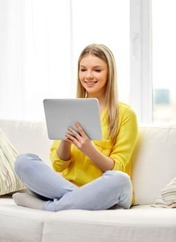people, technology and leisure concept - happy young woman or teenage girl sitting on sofa with tablet pc computer at home. young woman or teenage girl with tablet pc at home