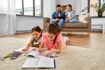 family, leisure and childhood concept - happy sisters lying on floor and drawing and doing homework at home. happy sisters drawing and doing homework at home