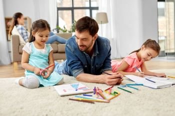 family, motherhood and leisure concept - father spending time with her little daughters drawing and helping with homework lying on floor at home. father spending time with little daughters at home