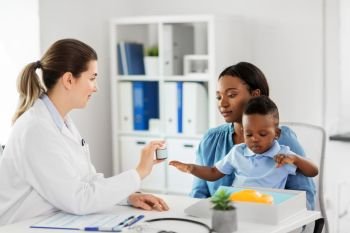 medicine, healthcare and pediatry concept - caucasian doctor giving medication to african american mother with baby son at clinic. doctor giving medicine to woman with son at clinic
